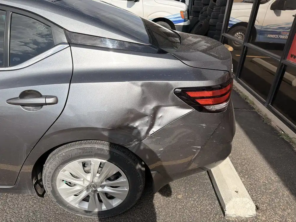 Gray sedan with a crushed rear quarter panel and scraped bumper before repair