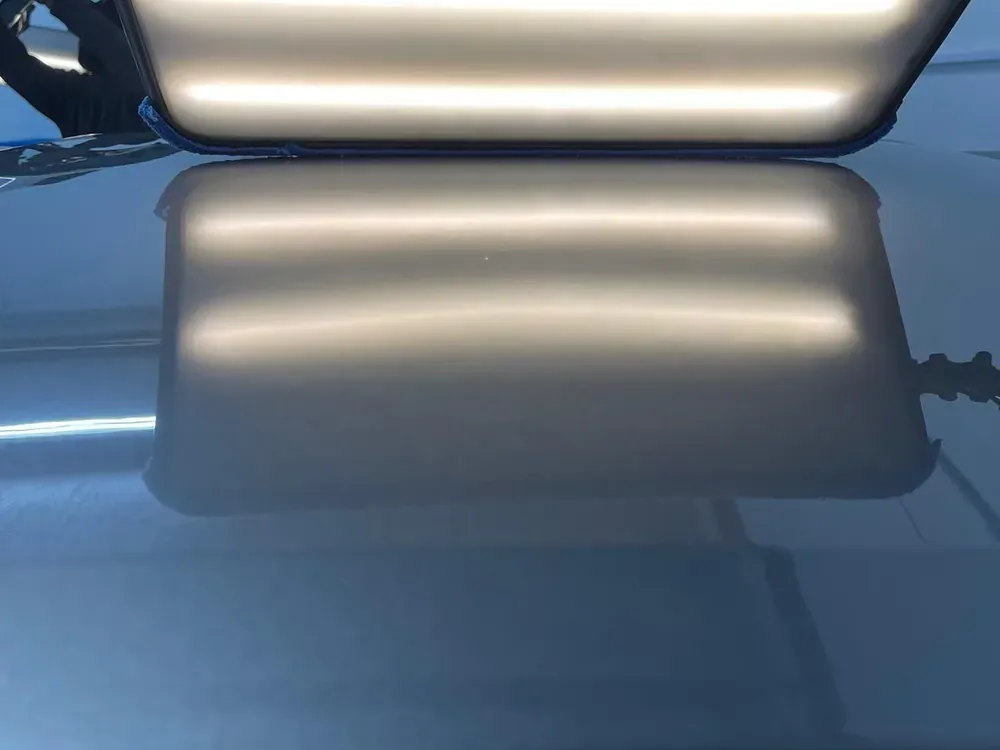 Dent repair light board held over a blue panel to read its surface
