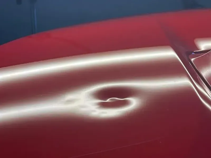 Light lines bending around a dent on a red car panel before repair