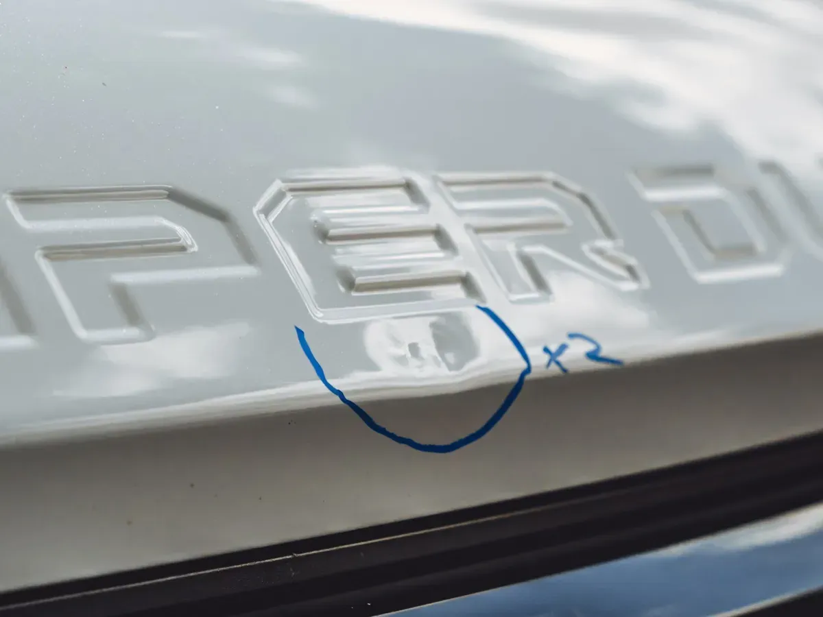 Close view of a hail dent circled in marker on a white Super Duty hood