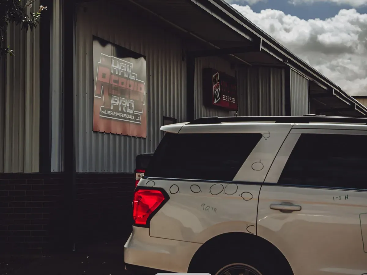 White SUV with marked hail dents parked outside the Hail Repair Pro shop building